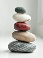 Kamienie ułożone jeden na drugim na drewnianym stole, reprezentujące spokój i stabilność.